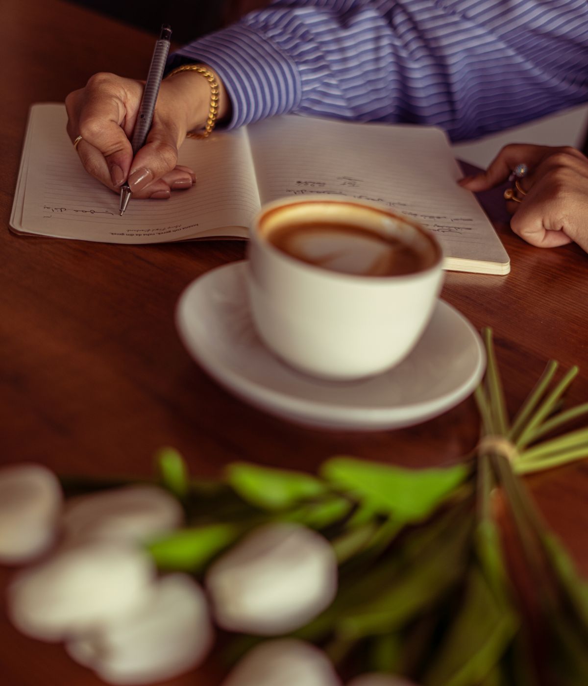 Mujer escribiendo en su diario junto a un café y tulipanes